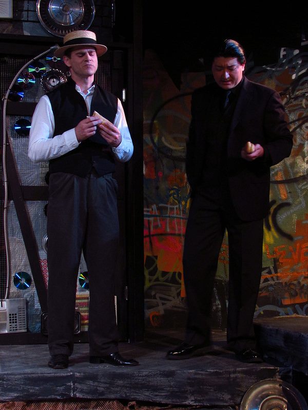 The factory owners (Will McMichael & Scot Shamblin) commiserate over the financial hit they took when they gave the women a raise... and plot to burn the factory down.
